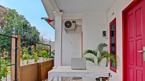 A small outdoor area with a white table, a red door, and a white wall with an air conditioning unit. - SPOT ON 91950 Guest House TekNong Syariah (Bangkinang)
