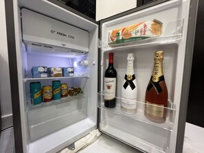 An open refrigerator with a 'FRESH ZONE' label, containing various beverages including beer, wine, and champagne.