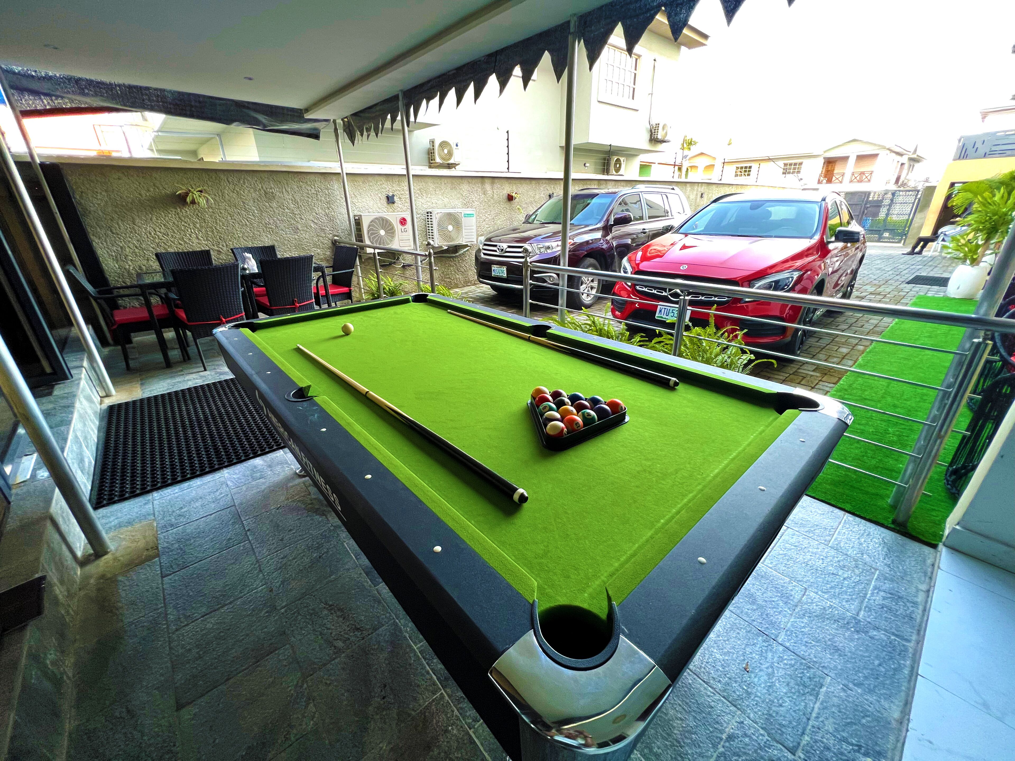 A pool table with balls, a red car, and a building in the background.