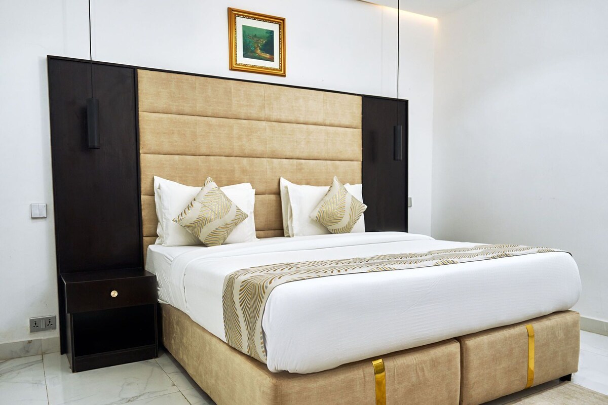 A modern bedroom with a large bed, a headboard, a nightstand, and a wall-mounted picture.