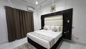 A bedroom with a large bed, a headboard, a bedside table, an air conditioning unit, a wall-mounted picture, and a window with curtains. - Riviera Lekki Resort (Lekki)
