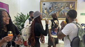 A group of people in a lobby with a large painting on the wall, a fire exit sign, and a potted plant. - Riviera Lekki Resort (Lekki)