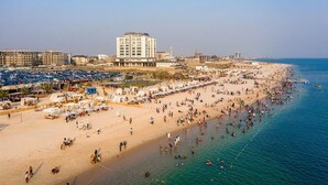 A beach with a hotel in the background, numerous beach umbrellas, and people enjoying the seaside. - Riviera Lekki Resort (Lekki)