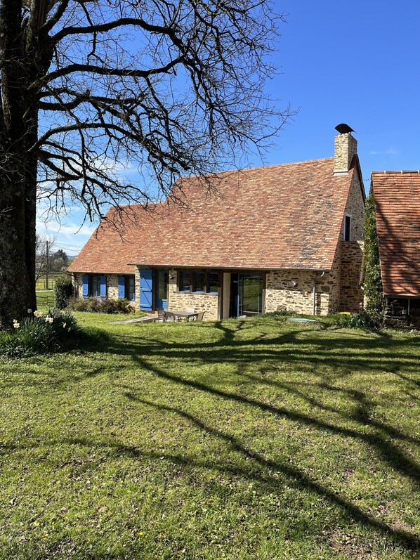 A stone house with a tiled roof, a small garden, and a clear blue sky.