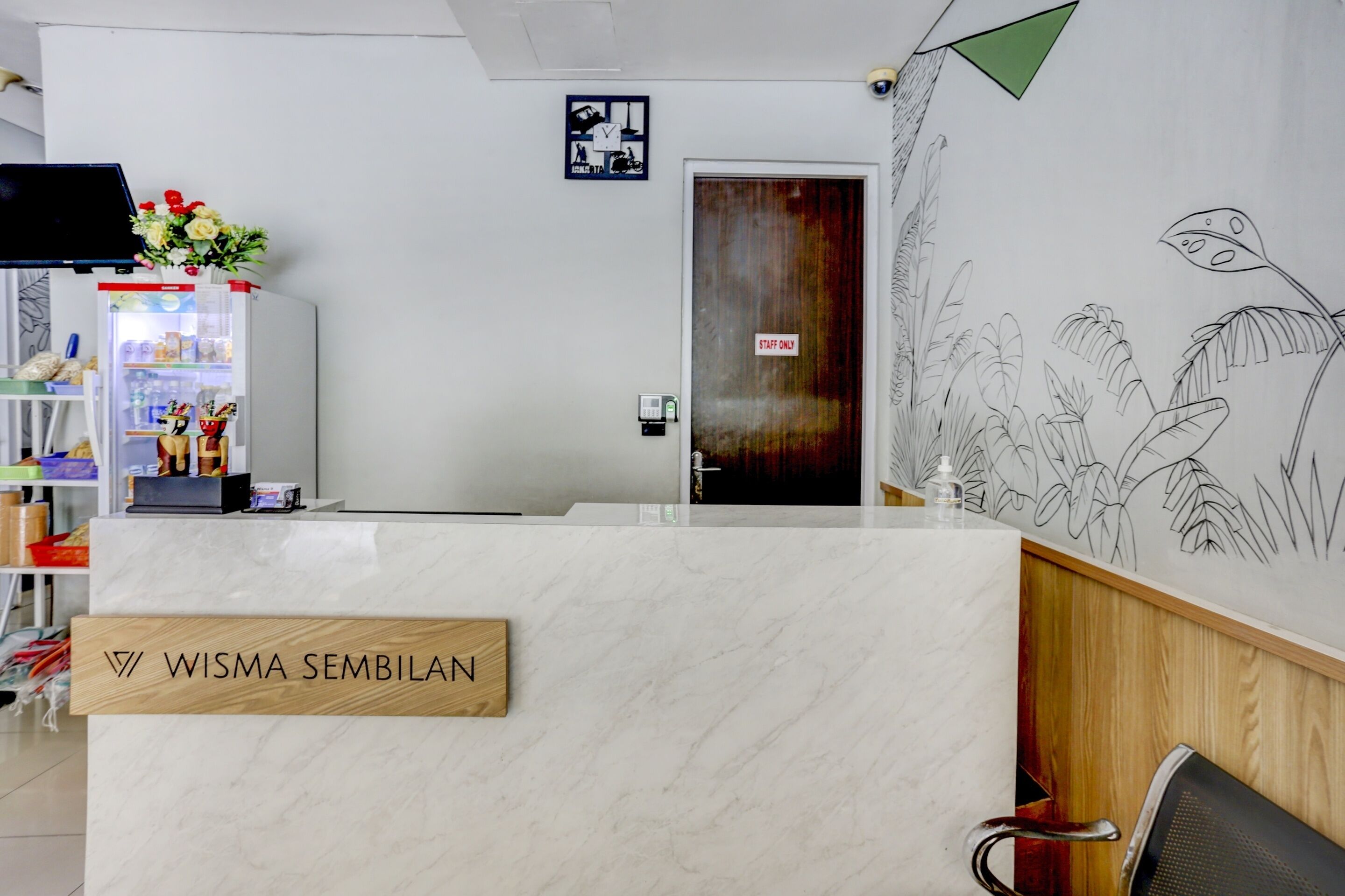 Un mostrador de recepción con un cartel que dice "WISMA SEMBILAN" y una puerta con la inscripción "SÓLO PERSONAL". 