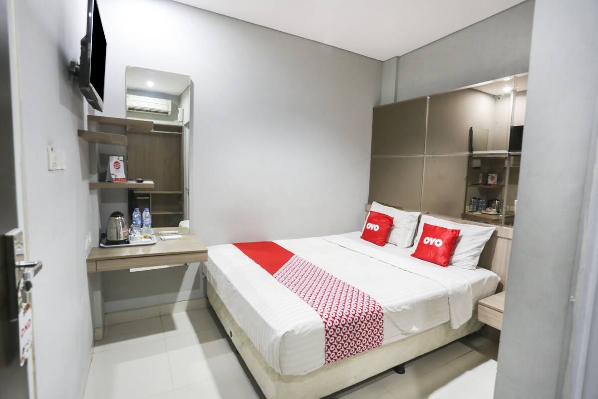 Una habitación de hotel moderna con cama, mesitas de noche, televisión y aire acondicionado integrado.