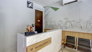 Un comptoir d’accueil avec une plaque portant l’inscription « Wisma Sembilan », une porte en bois et un mur orné d’un motif de feuilles.