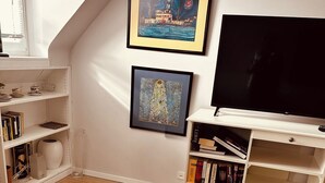 A cozy living room with a white sofa, a pink knitted throw, a bookshelf, a flat-screen TV, and two framed artworks on the wall. - Casa Neuenheim (Heidelberg)