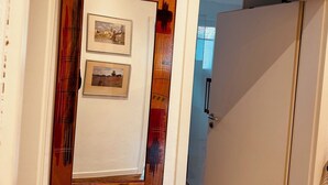 A hallway with a door featuring a wooden frame and two framed pictures. An air conditioning unit is mounted above the door. - Casa Neuenheim (Heidelberg)