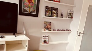 A room with a white TV stand, a framed picture, and a bookshelf with books. - Casa Neuenheim (Heidelberg)