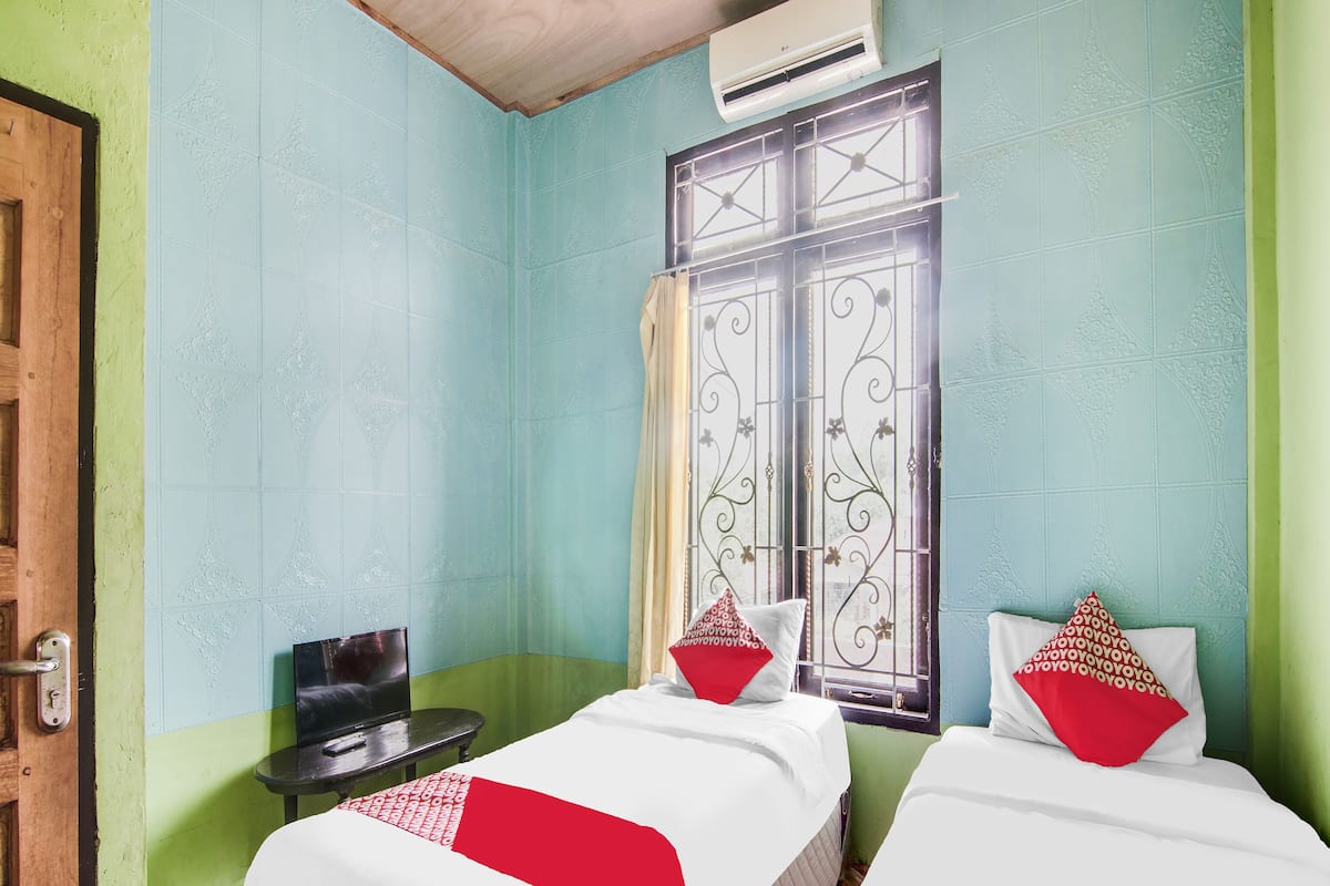 Una habitación con dos camas, una mesita, una ventana con rejas decorativas y un equipo de aire acondicionado.