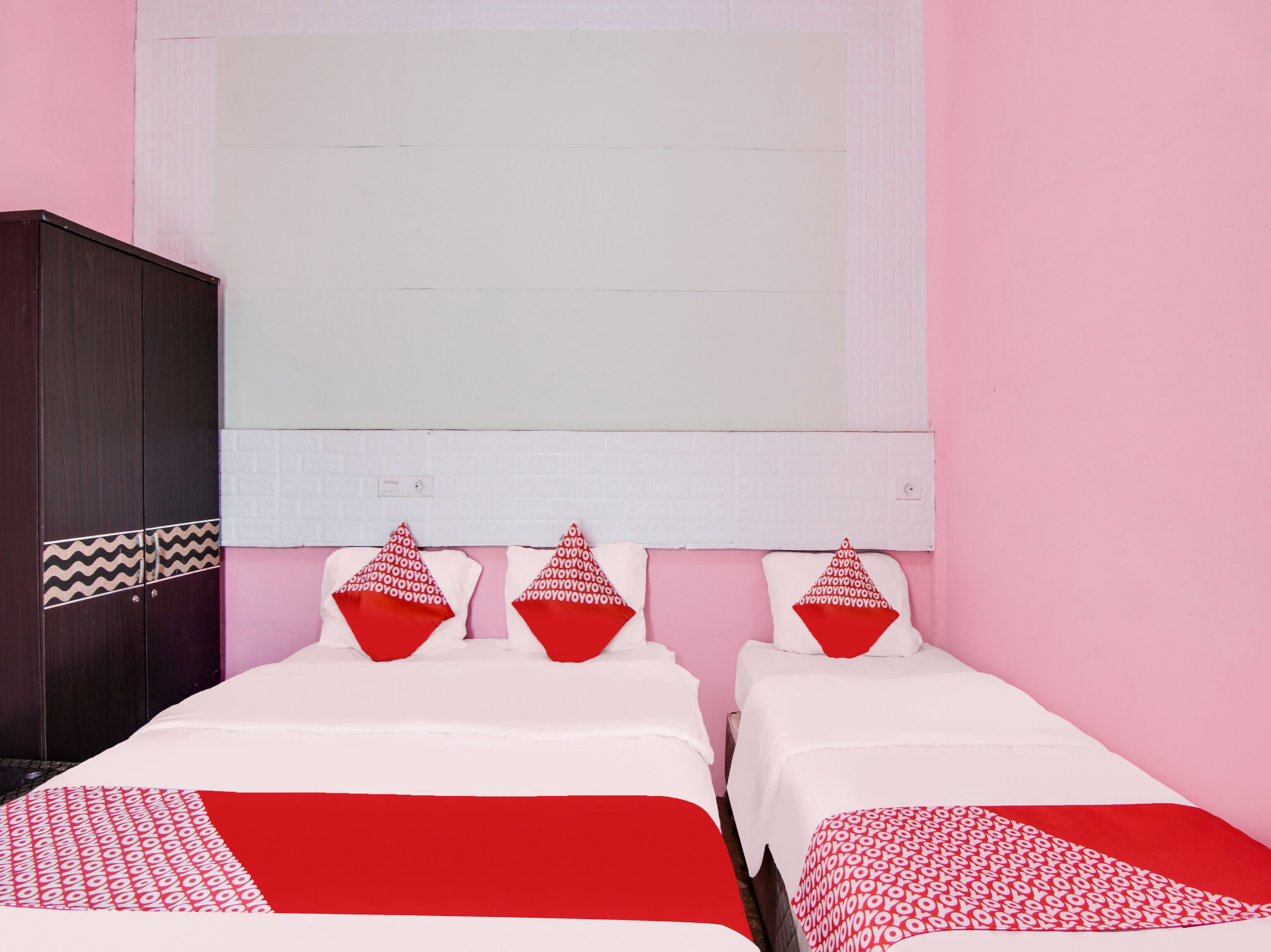 Een kamer met twee bedden, elk met een rood-wit gebedde en drie rode en witte kussens.