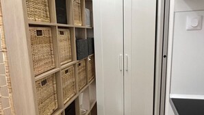 A narrow hallway with a white wardrobe, wicker baskets on shelves, and a striped rug.