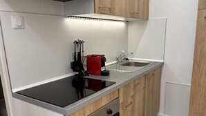 A compact kitchen with a black countertop, wooden cabinets, a built-in oven, and a stainless steel sink.