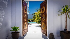 A pathway leading to a pool area with ornate wooden doors, potted plants, and a clear blue sky.