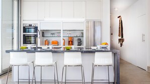 A modern kitchen with a central island, bar stools, a built-in oven, and a coffee station.