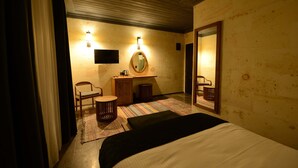 Une chambre d’hôtel comprenant un lit, un bureau avec une chaise, une petite table, un miroir et un luminaire fixé au mur.