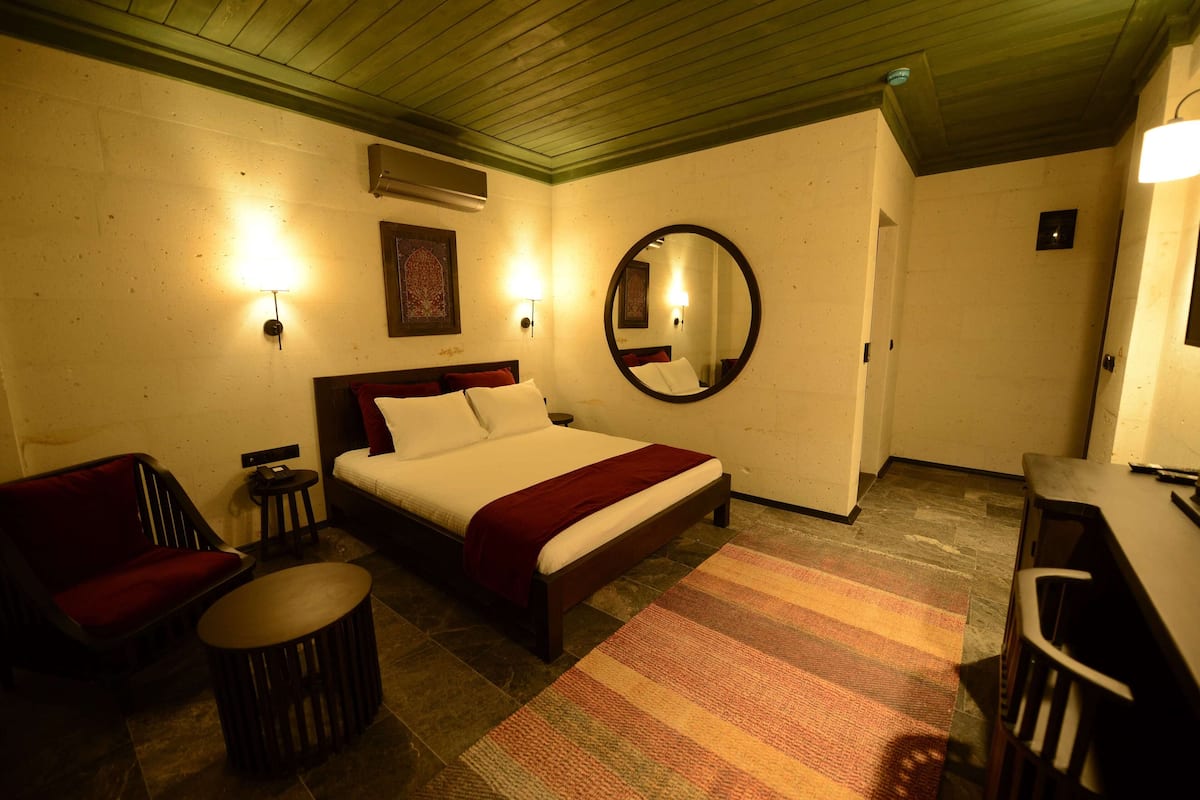 Una habitación de hotel con cama, una silla, una mesita, un espejo y luces en la pared.