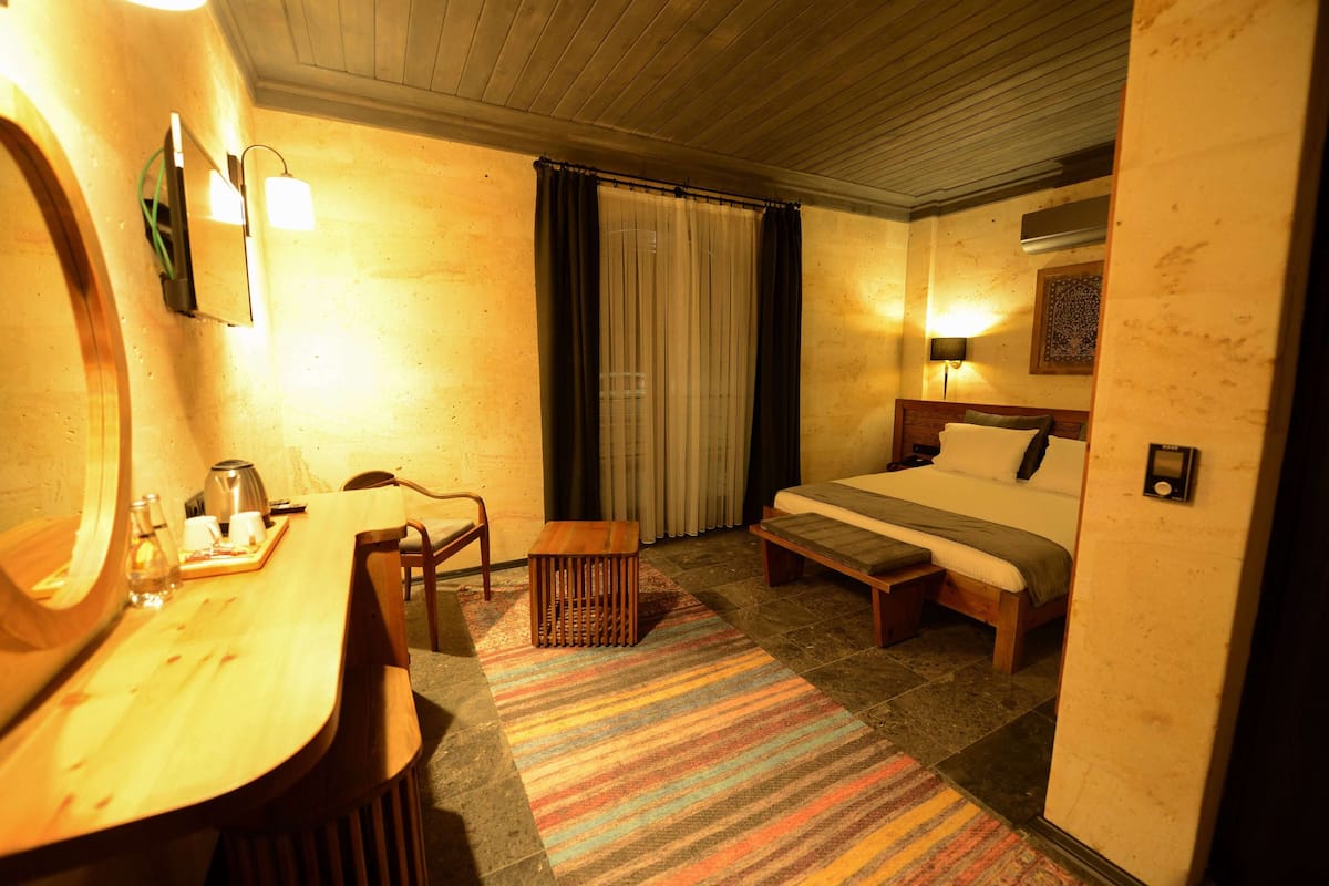 Habitación de hotel con escritorio de madera, cama con alfombra a rayas, una silla y un espejo.