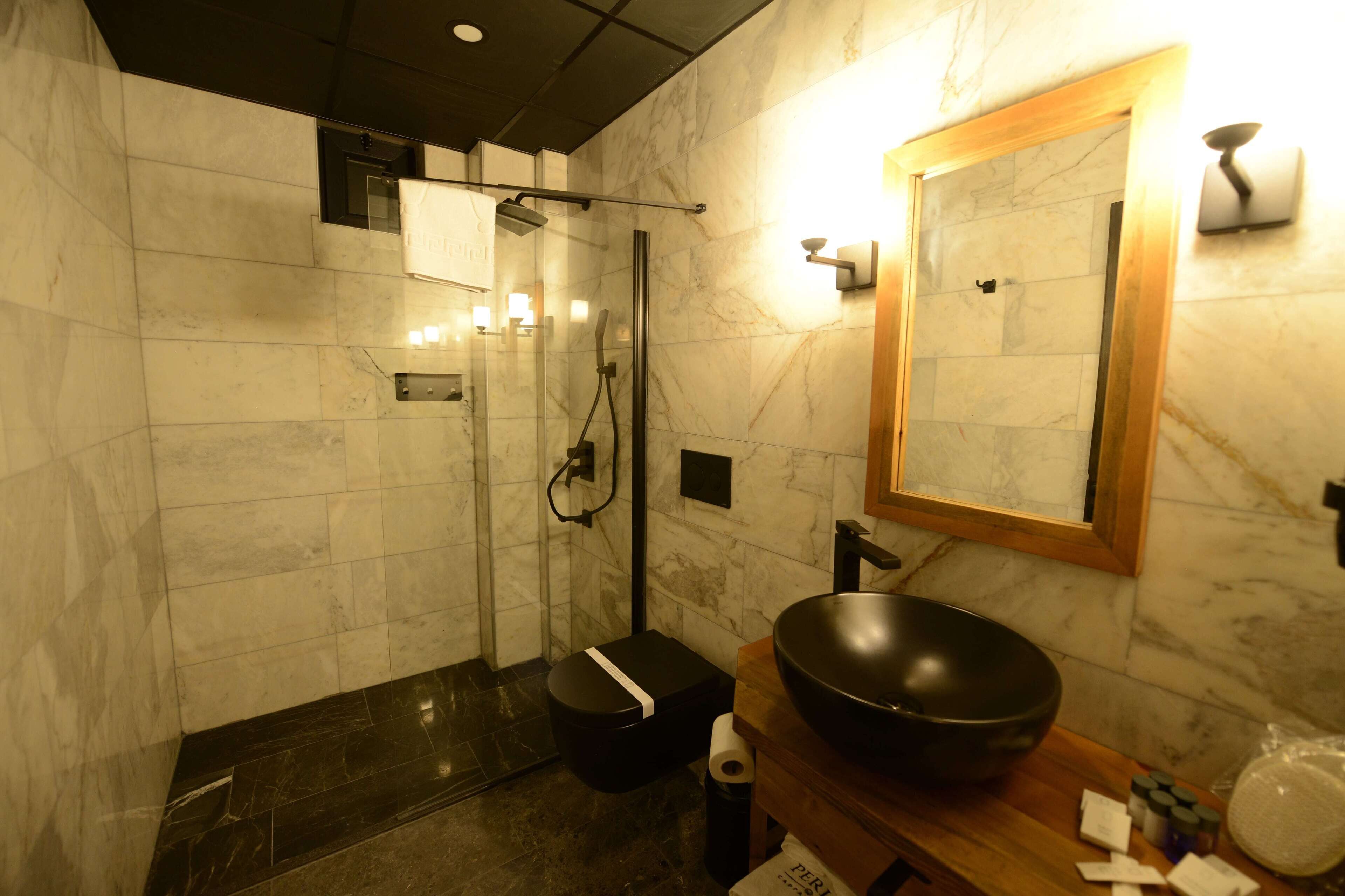 A modern bathroom with a glass-enclosed shower, a black sink with a large basin, and marble walls.