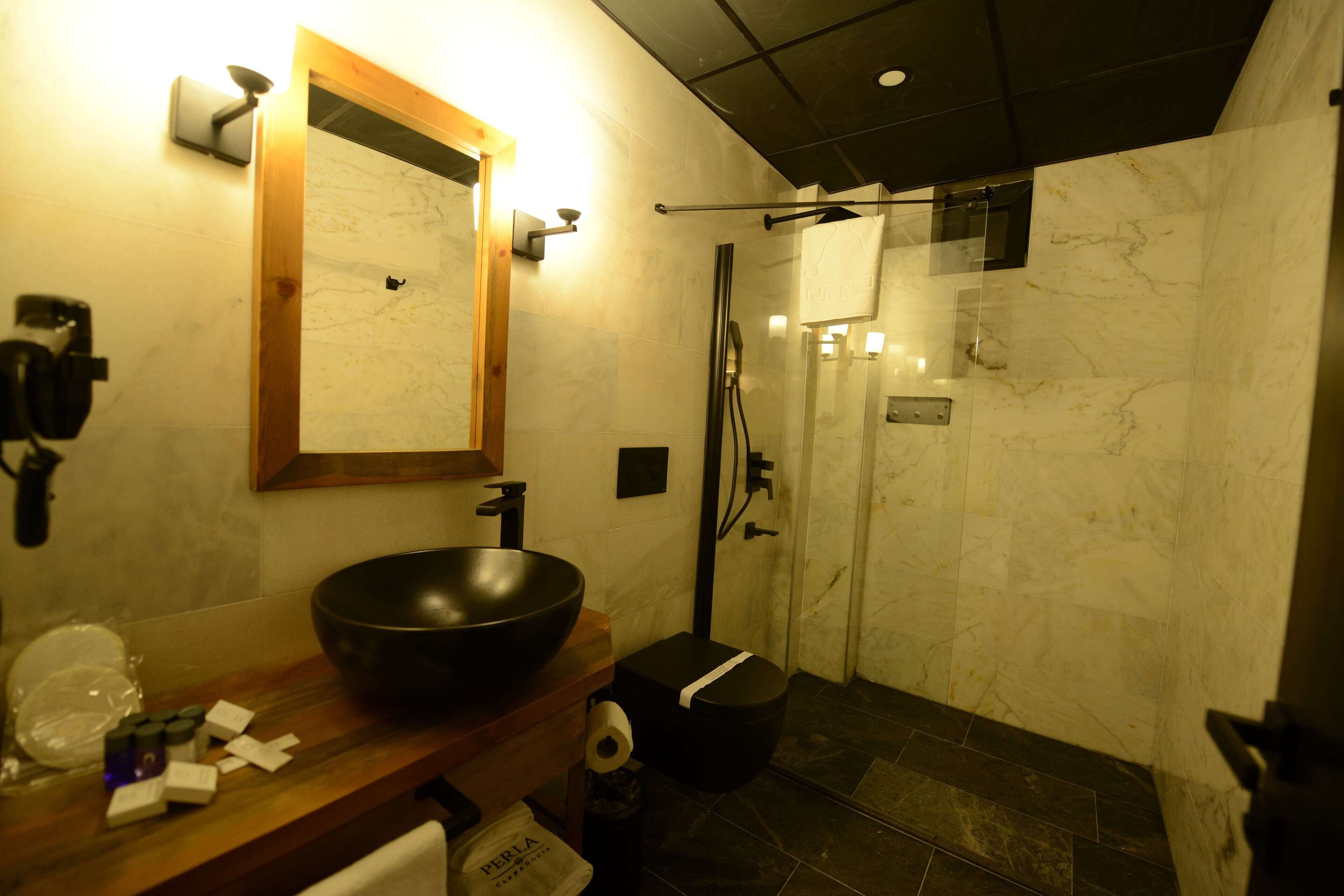 A modern bathroom with a large black basin, a wooden countertop, a mirror, and a glass-enclosed shower area.