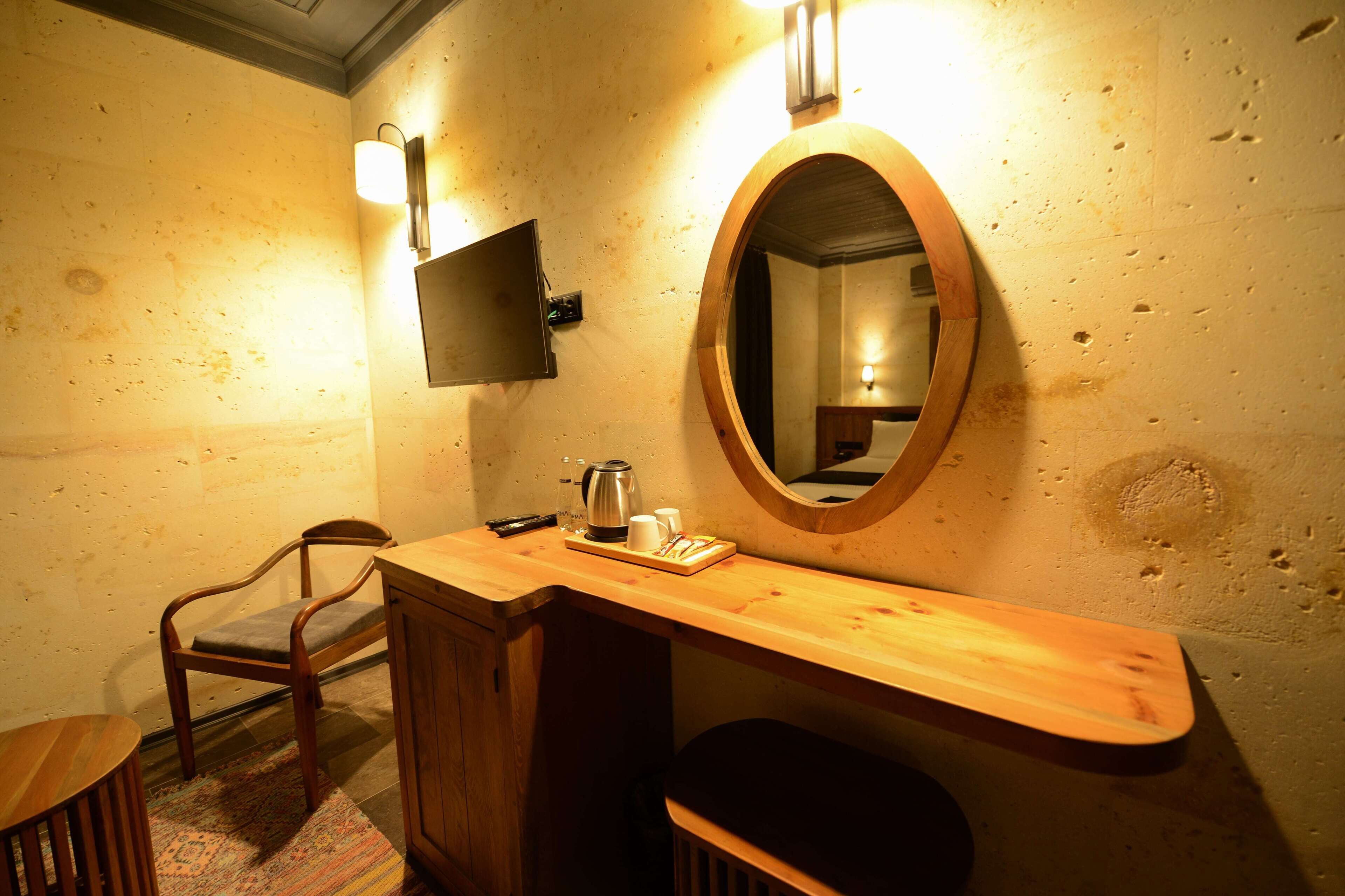 A wooden vanity with a mirror, a chair, and a small table with a kettle and cups.