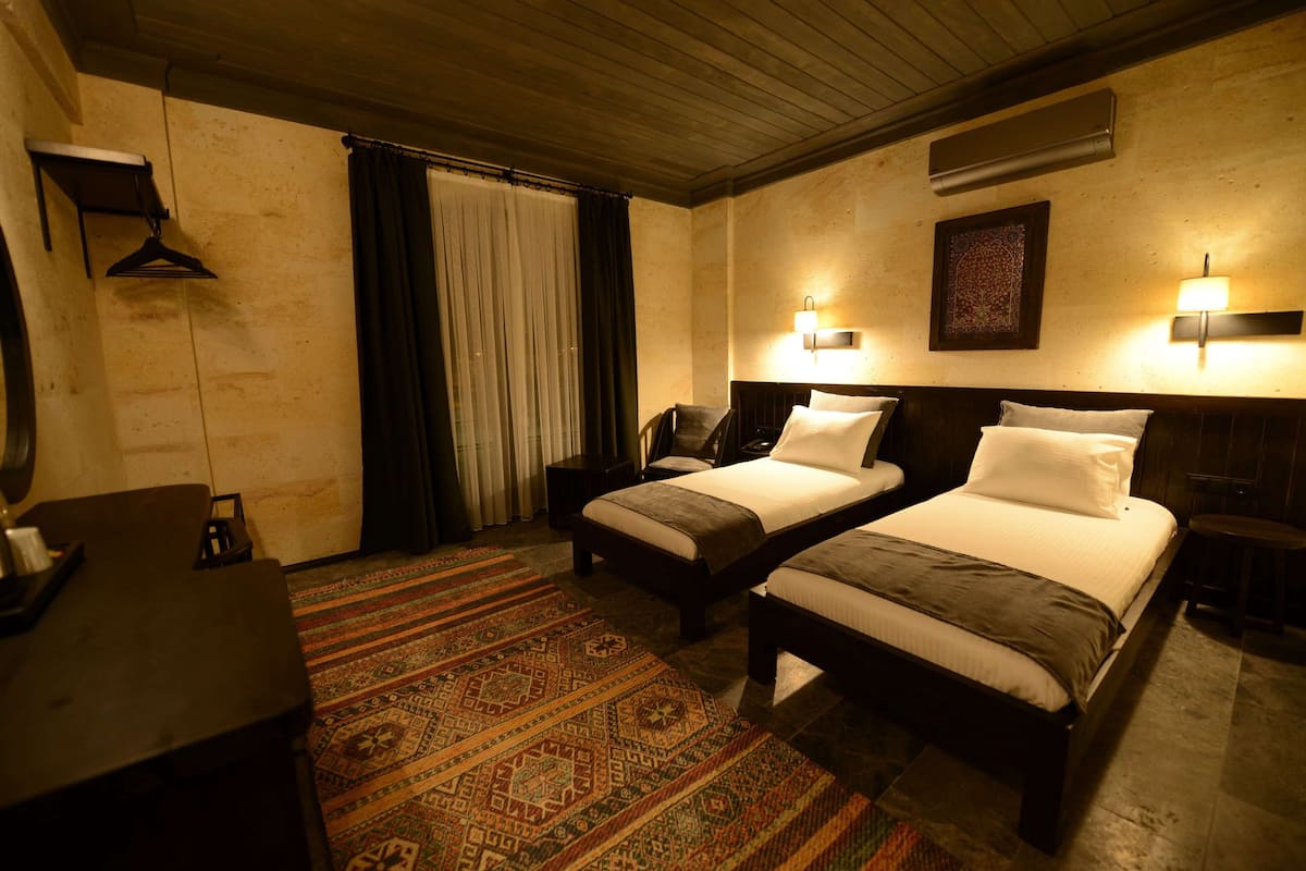 Habitación de hotel con dos camas, un escritorio, perchero y alfombra estampada.