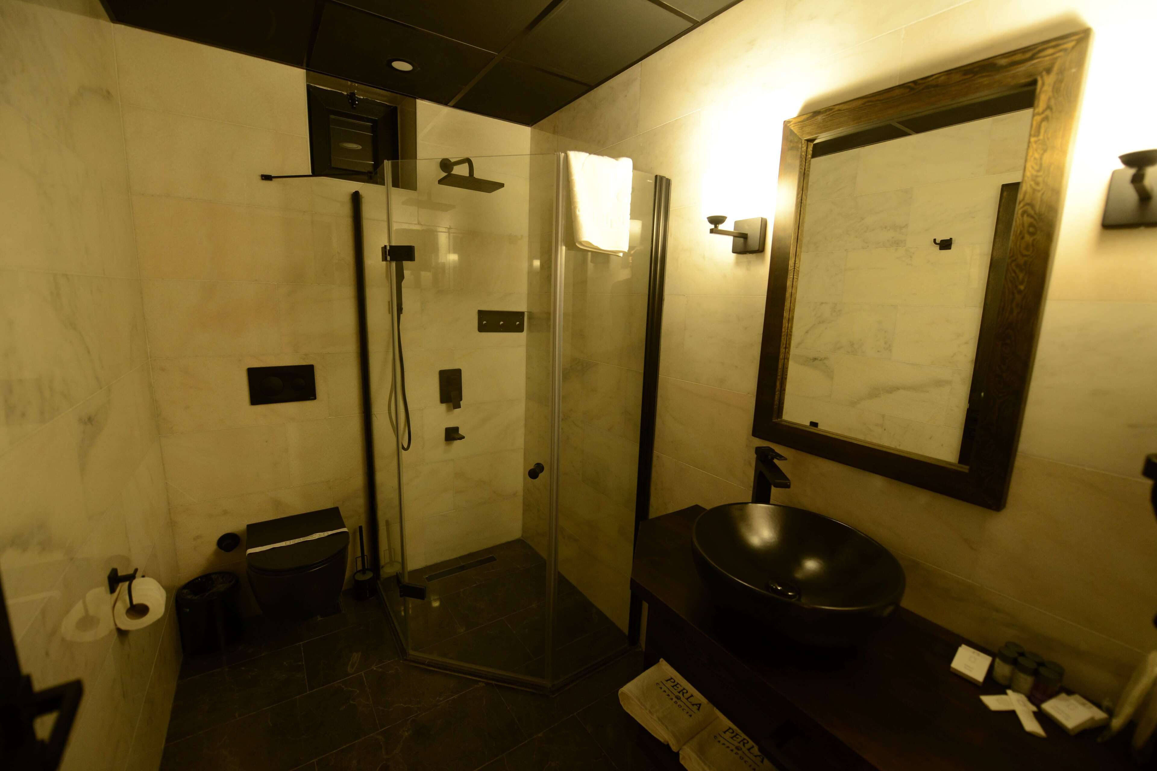 Un baño moderno con ducha envuelta en vidrio, lavabo negro y un espejo grande.