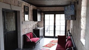 A rustic room with stone walls, a wooden ceiling, a red sofa, a red chair, a small table, and a window with a view.
