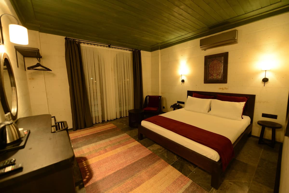 Habitación de hotel con cama, escritorio, silla, perchero y aire acondicionado instalado en la pared.