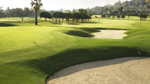 Campo de golf con un búnker de arena, árboles y cielo despejado.