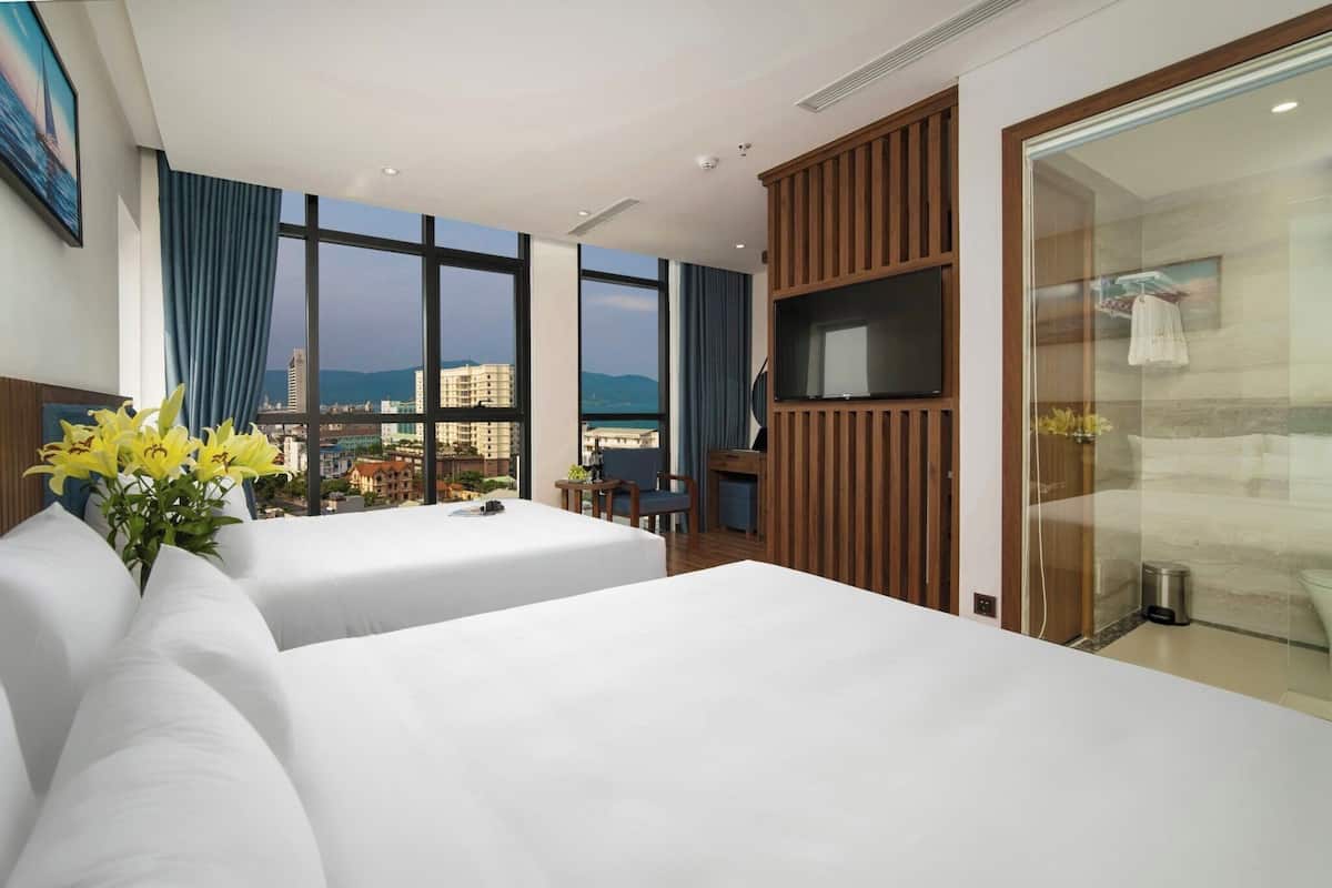 A hotel room with two beds, a TV, a desk, and a view of the city.