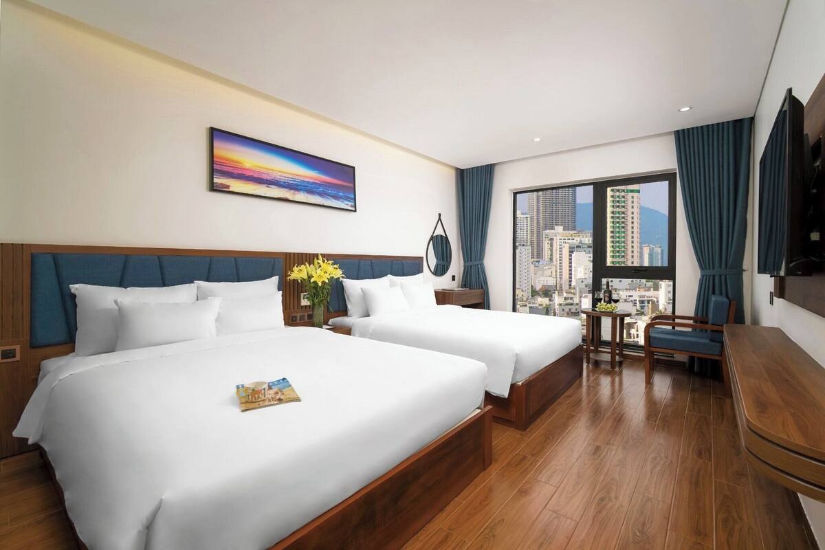 A hotel room with two beds, a city view, a painting, and a small table with flowers.