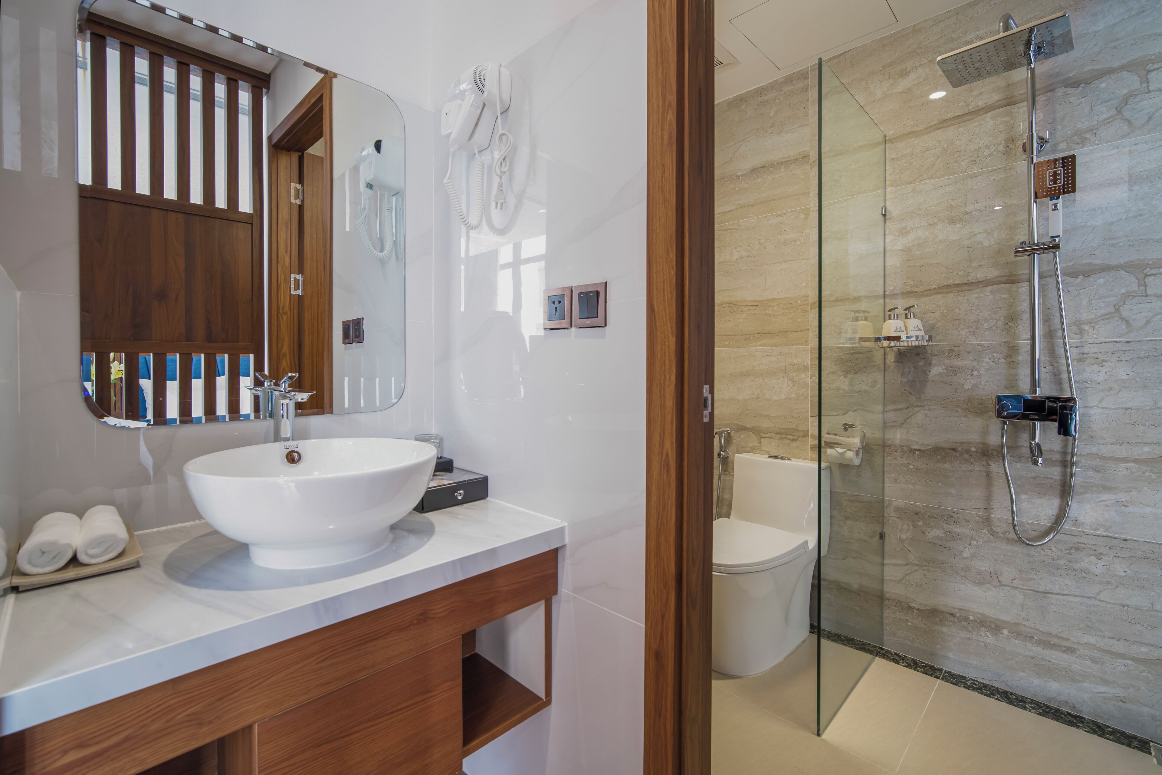 A modern bathroom with a large white sink, a wooden vanity, a glass-enclosed shower, and a toilet.