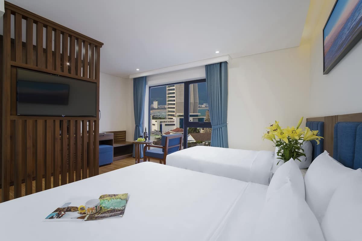 A hotel room with two beds, a TV, a desk, and a view of the city.