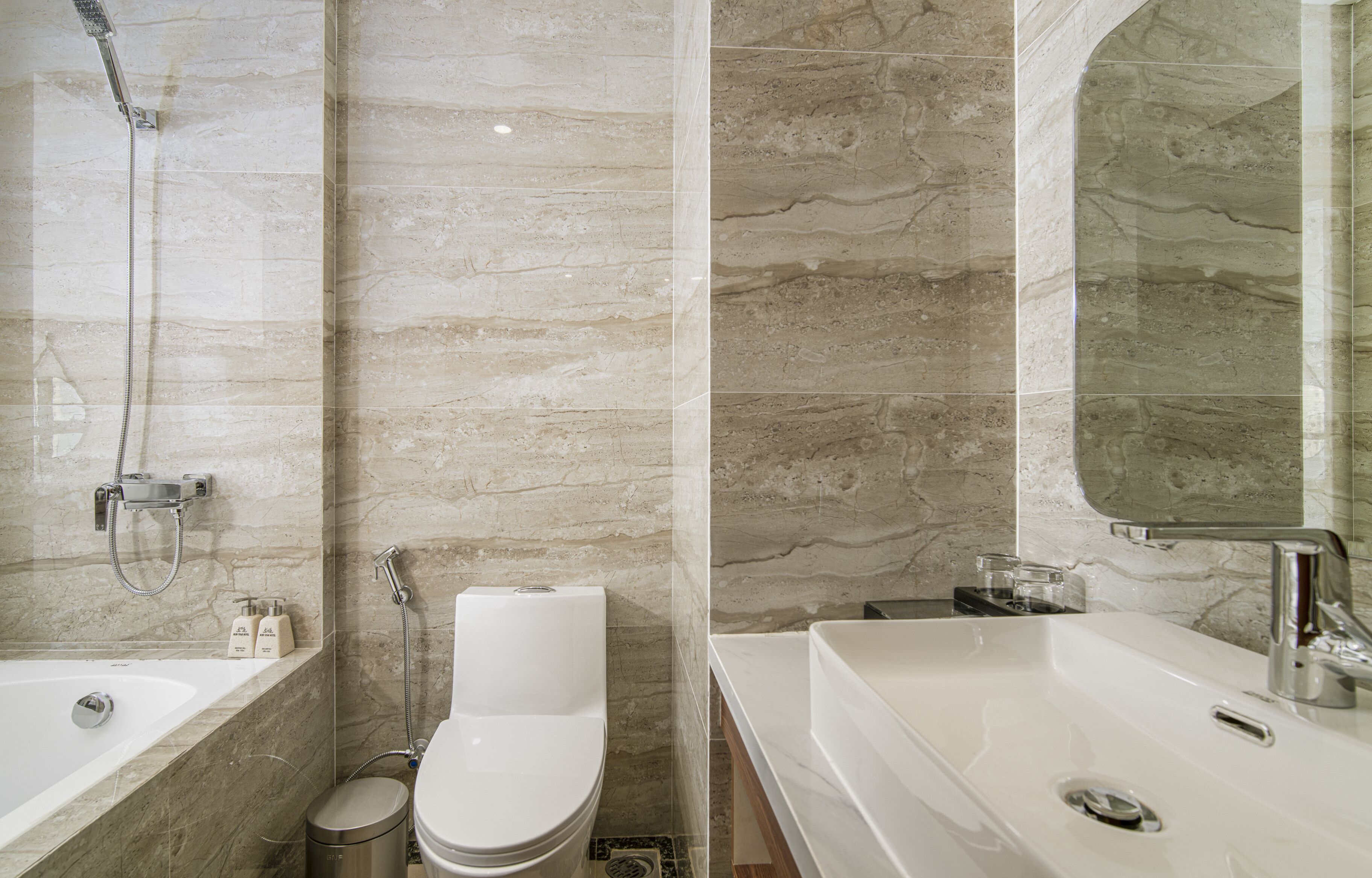 Un bagno moderno con vasca, water e lavandino, caratterizzato da pareti in marmo e un ampio specchio.