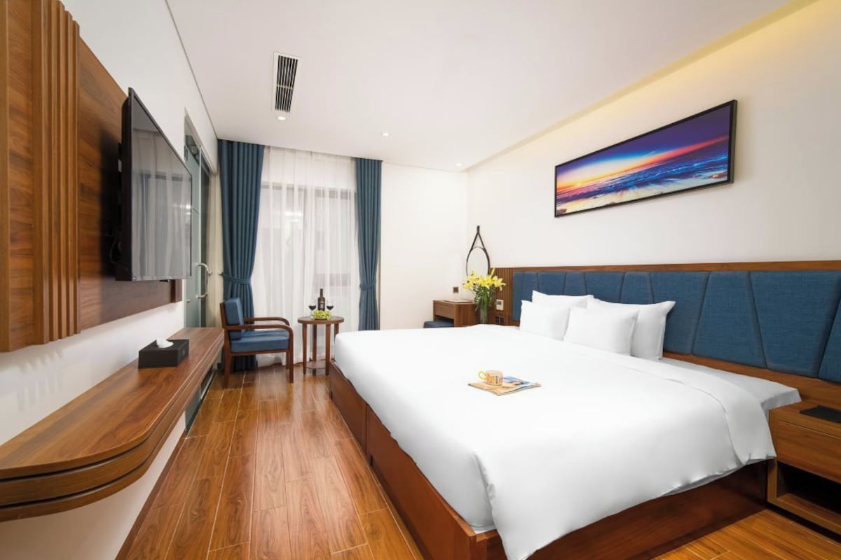A hotel room with a large bed, a TV, a desk, and a window with curtains.