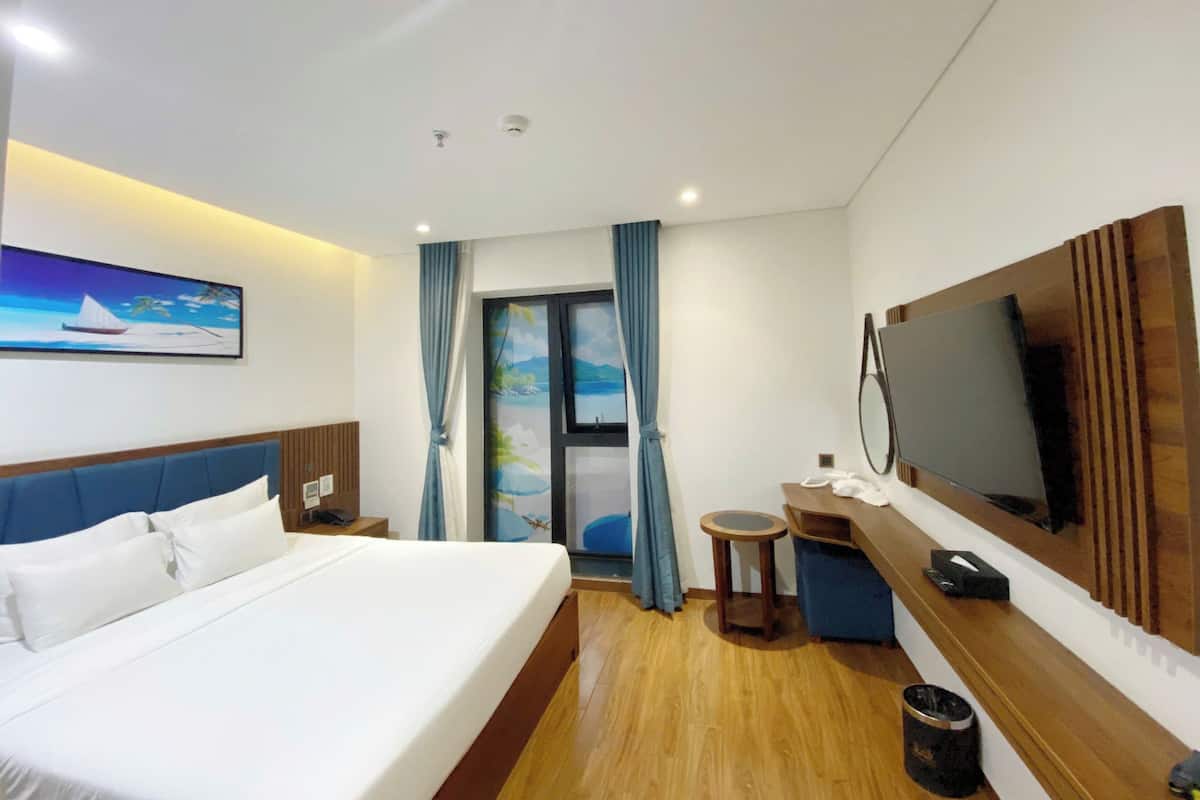 A hotel room with a bed, a desk, a television, and a window with curtains.