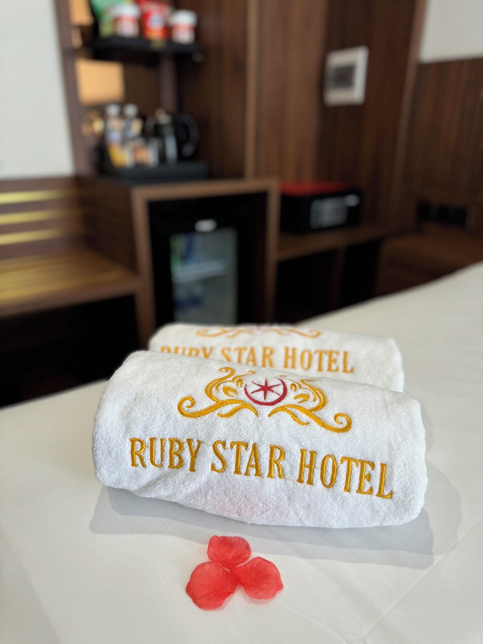 Un letto con un asciugamano bianco con ricamo dorato 'Ruby Star Hotel'.