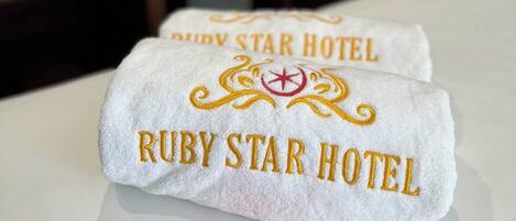Un letto con un asciugamano bianco con ricamo dorato 'Ruby Star Hotel'.