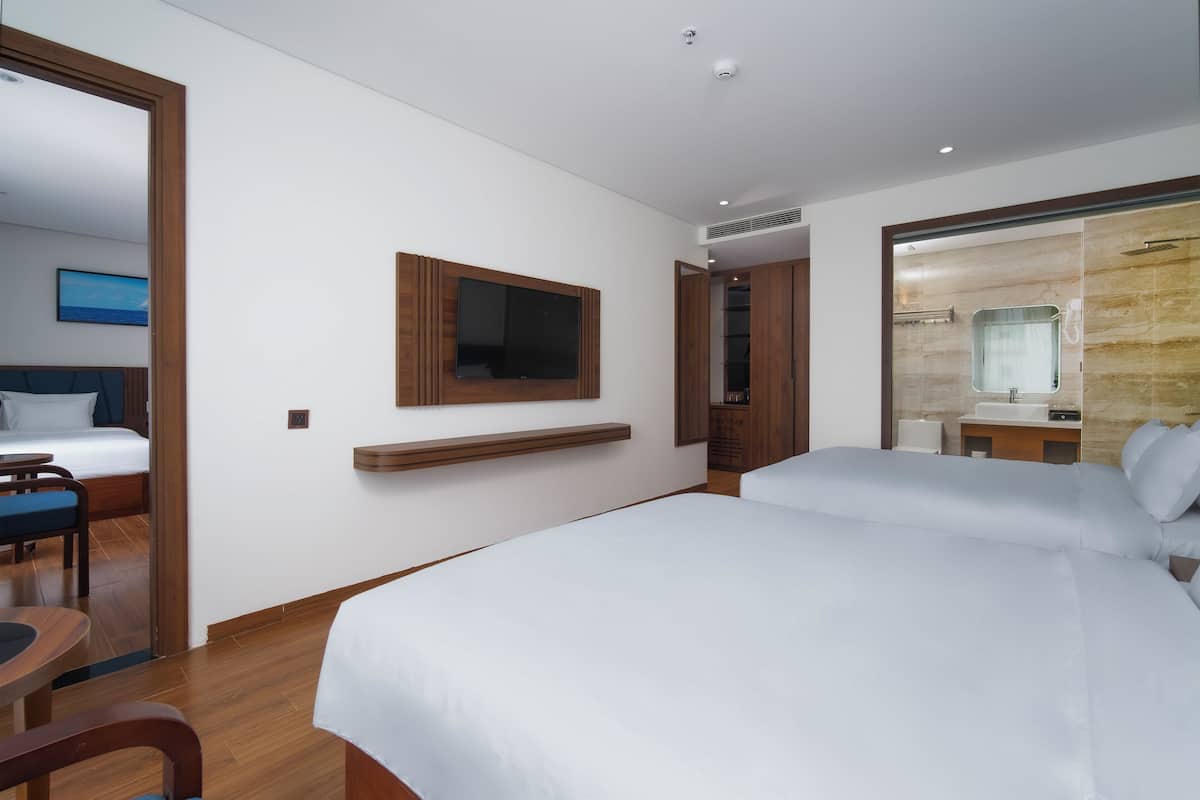 A hotel room with two beds, a TV, a mirror, a wooden floor, and a bathroom with a shower.