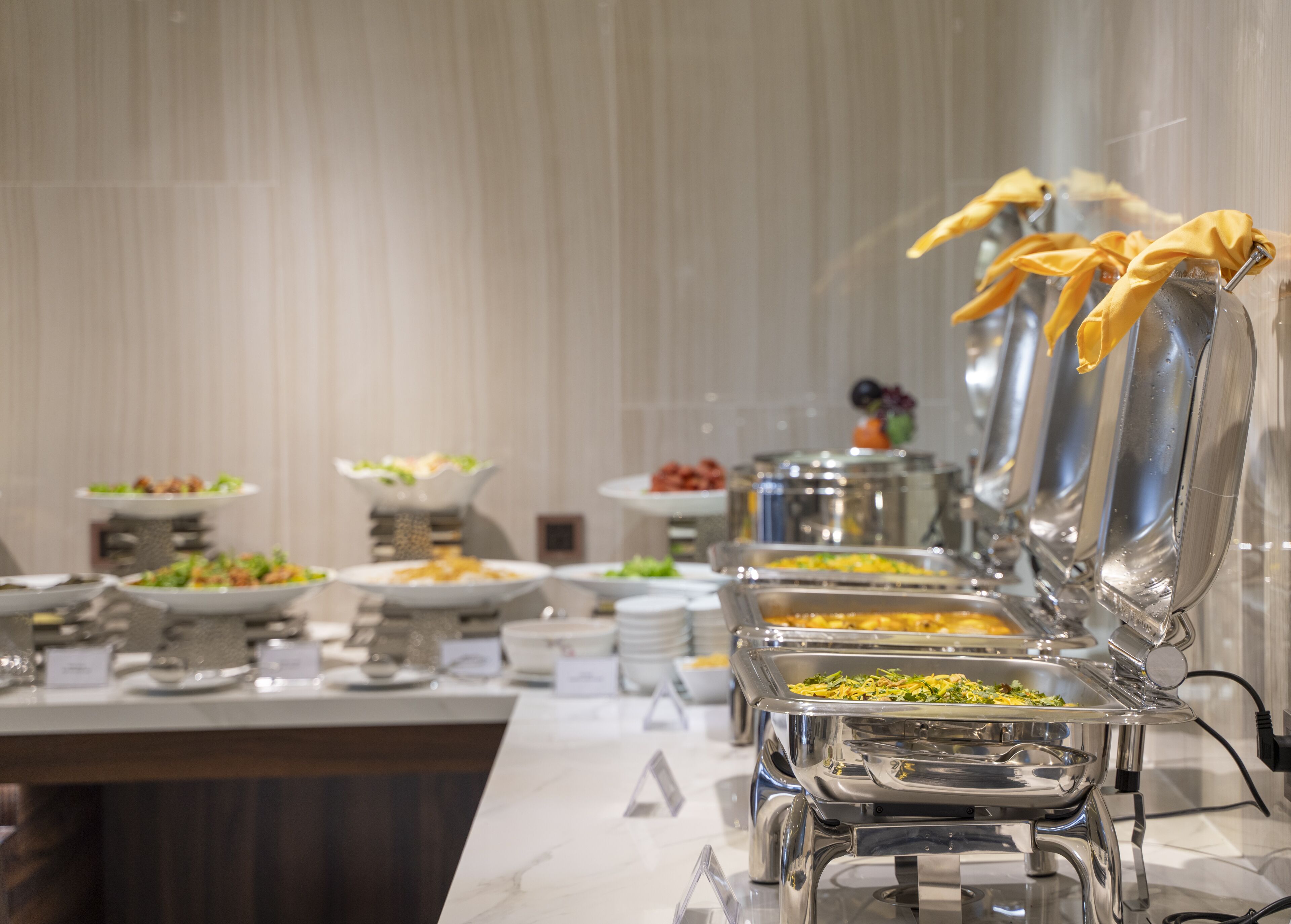 A buffet setup with multiple serving stations, each with a covered dish and a yellow cloth.