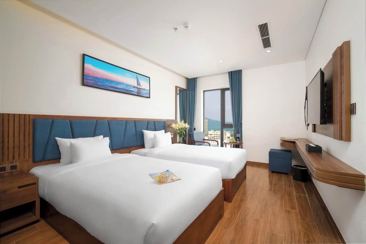 A hotel room with two beds, a large window, a TV, and a painting of a sailboat.