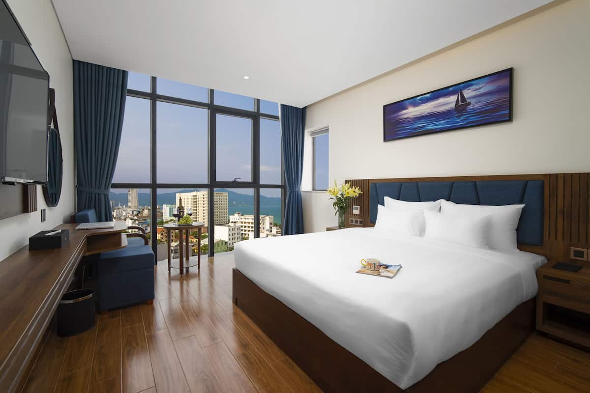 A modern hotel room with a large bed, a desk, and a view of the city.