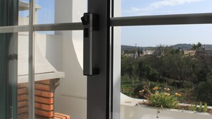 A balcony with a view of a residential area, a brick bench, and a glass door with a handle.