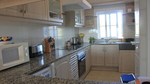 A kitchen with granite countertops, white cabinets, a microwave, a coffee maker, and a sink.