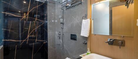Un baño moderno con cabina de ducha de vidrio, inodoro blanco, lavamanos grande y tocador de madera.