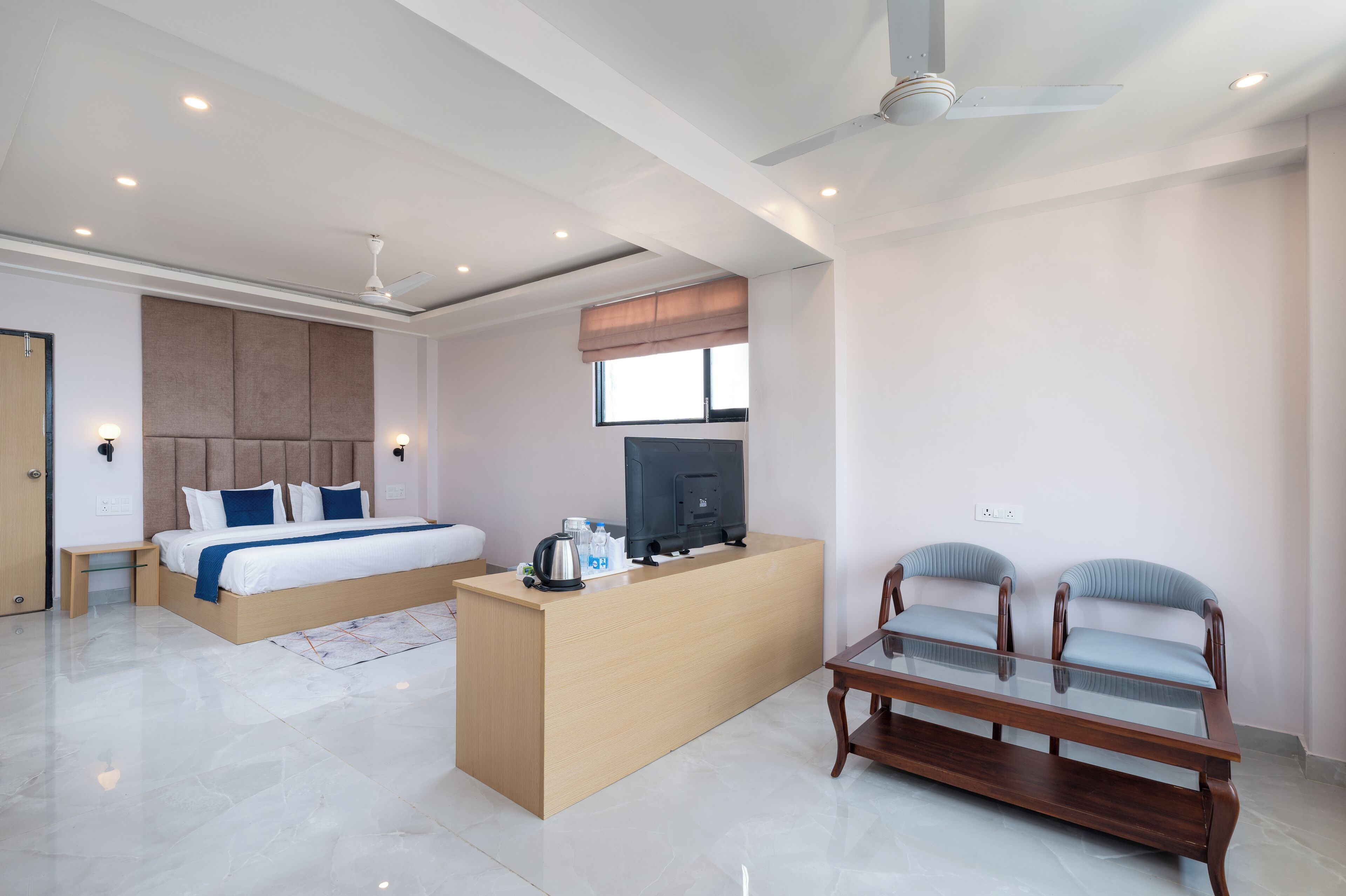 A modern hotel room with a bed, a desk, a TV, and two chairs.
