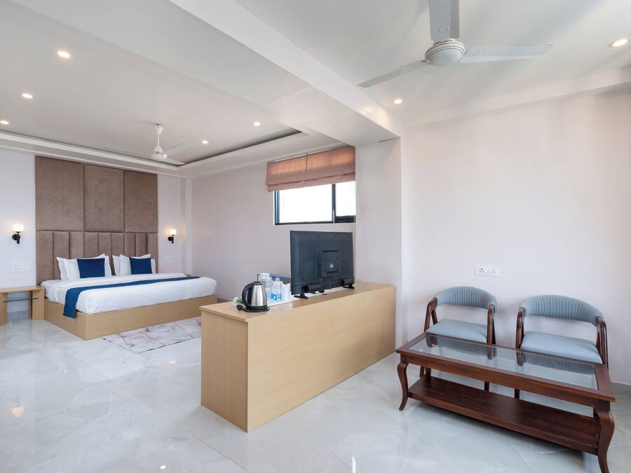 A modern hotel room with a bed, a desk, a TV, and two chairs.