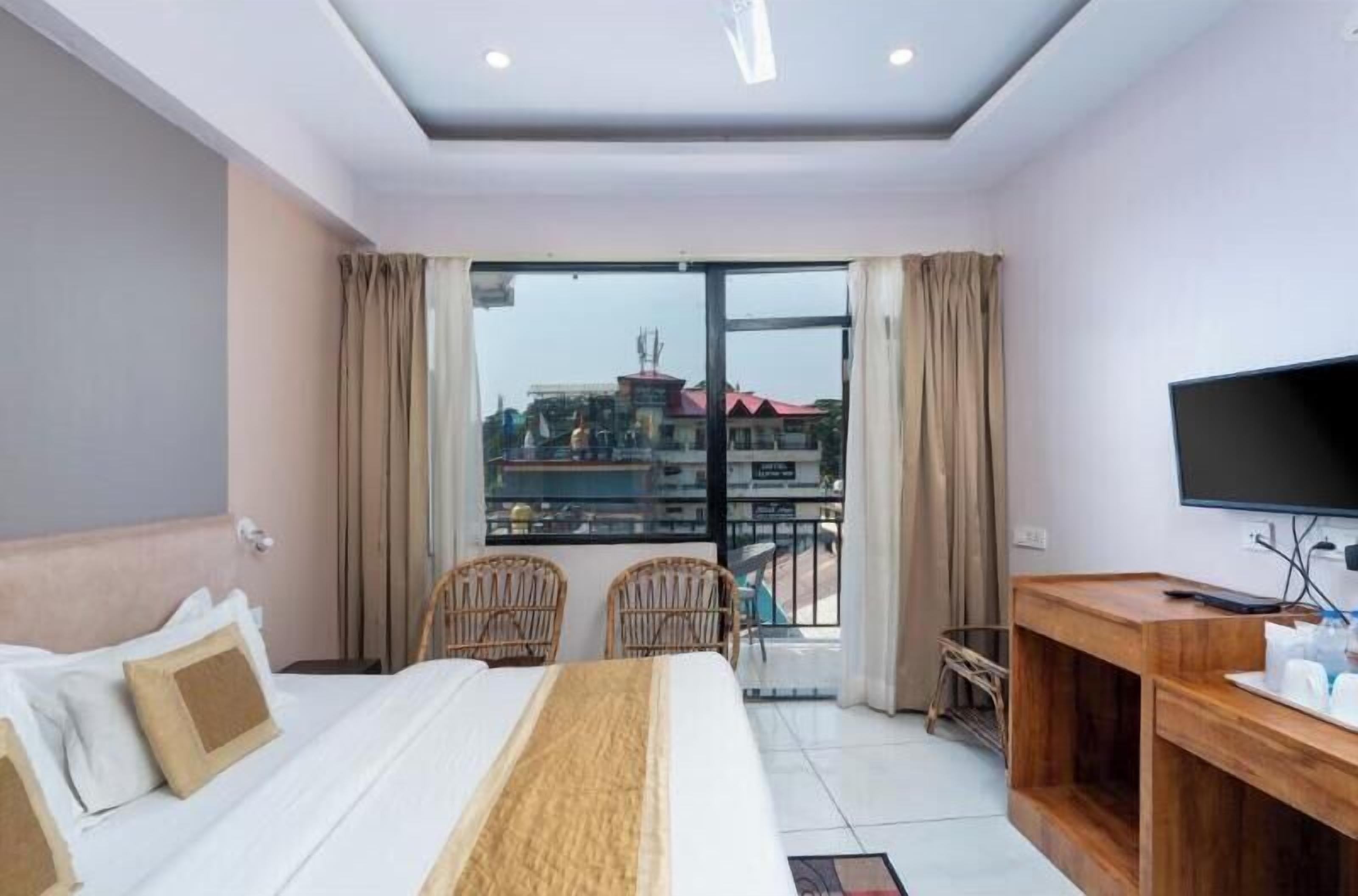 A hotel room with a bed, a TV, a desk, and a balcony with a view of buildings.
